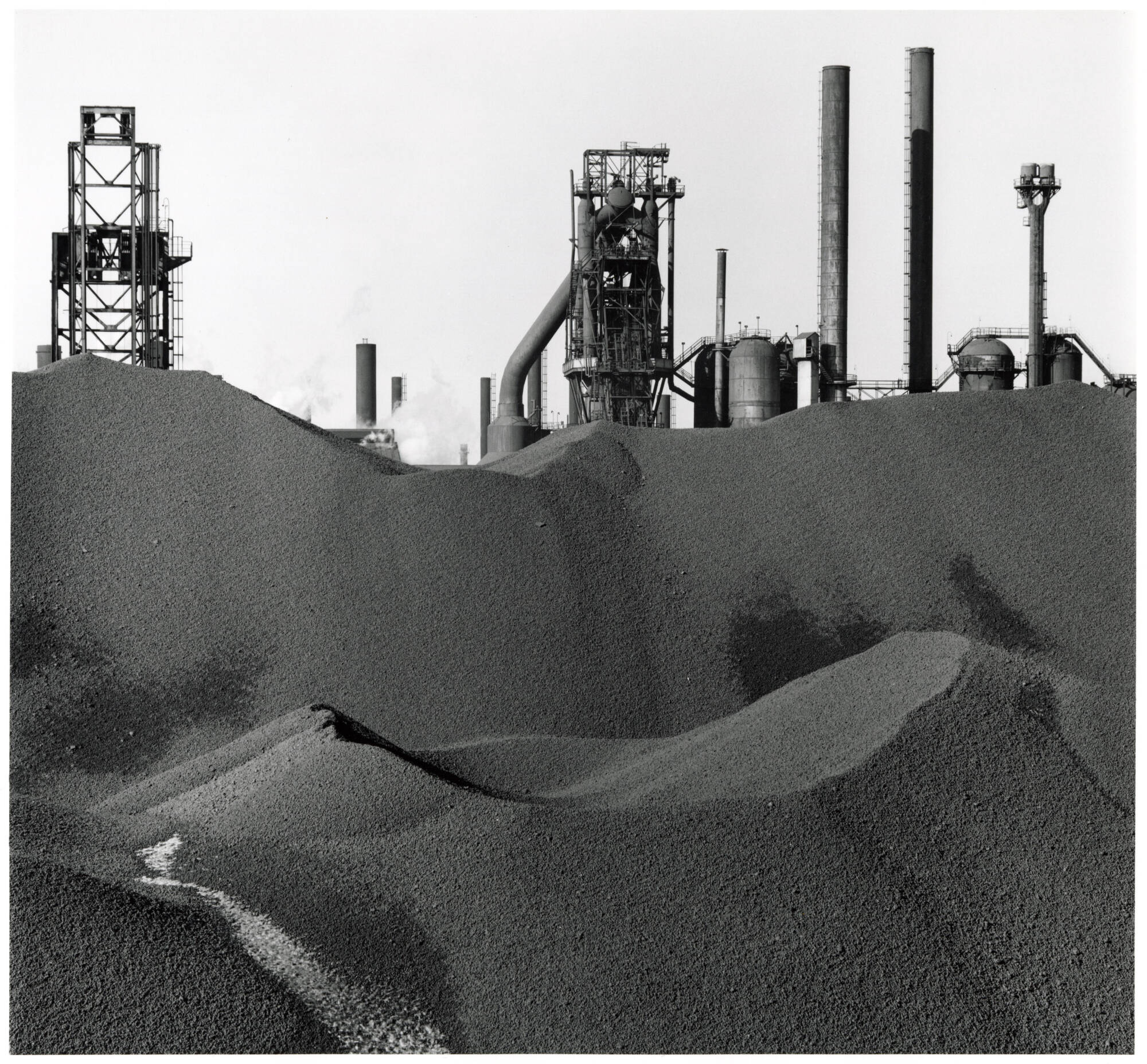 Black and white photograph of digging pits with machines at top of man-made hills.